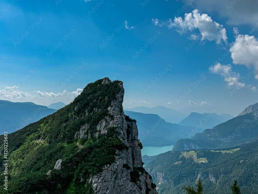 Fototapeta premium Majestic rugged sharp rock formation overlooking alpine lake Lago di Molveno in valley Andalo Paganella, Trentino, Italy. Surrounded by pristine wild mountain range of Brenta Dolomites, Italian Alps