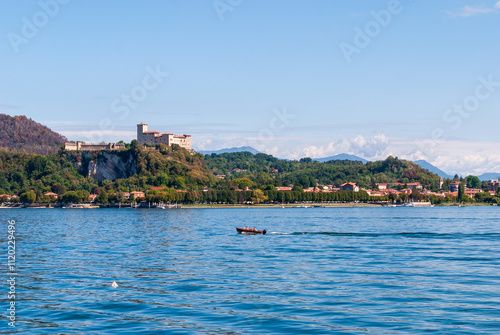 From Arona, the Rocca di Angera rises majestically above Lake Maggiore, its medieval fortress perched on a hill, offering a stunning contrast to the serene waters below. photo