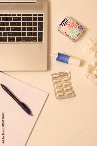 Working while sick; In the background there is a laptop, notebook, tissues, nasal spray and pills
