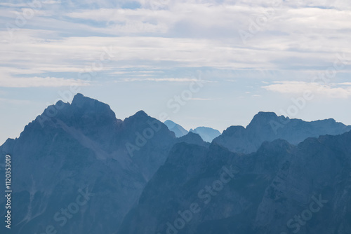 Silhouette of majestic mountain peak Jalovec in pristine Julian Alps. On top of Cima Del Lago on border Italy Slovenia, Triglav National Park. Wanderlust in alpine wilderness. Misty atmosphere photo