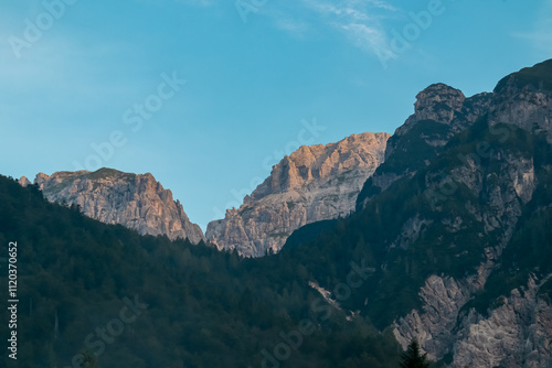 Scenic view of majestic mountain peak of Mangart in Julian Alps seen from Predil Pass, Tarvisio, Italy. Ridges covered in morning mist. Hiking trail on alpine terrain covered with conifer forest