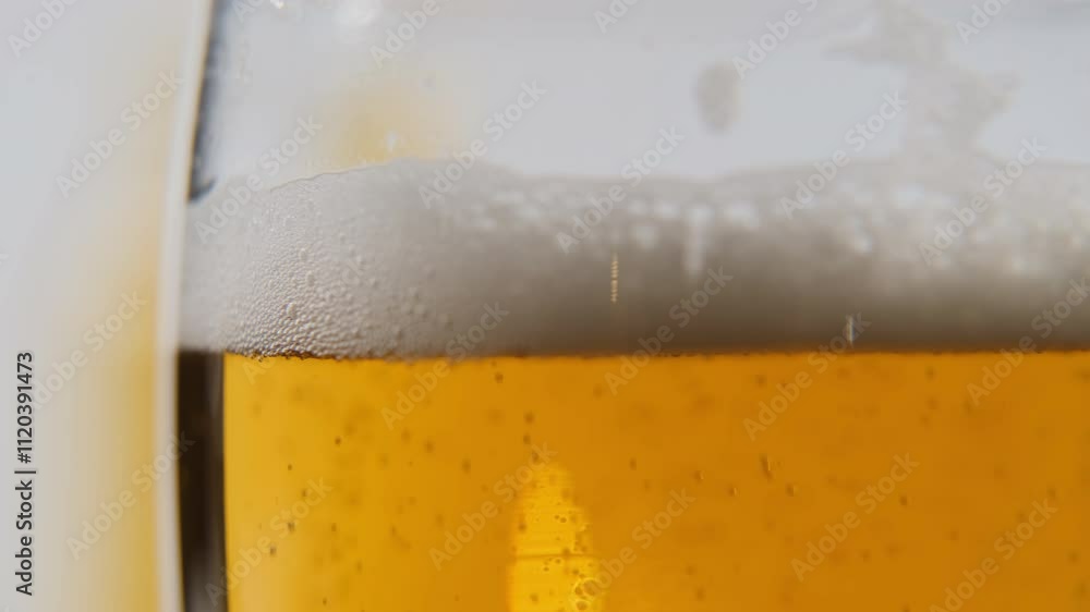 Close-up view reveals a glass brimming with freshly poured beer, golden yellow and topped with a rich, foamy head and bubbles rising Close-up view reveals a glass brimming with freshly poured beer, golden yellow and topped with a rich, foamy head and bubbles rising