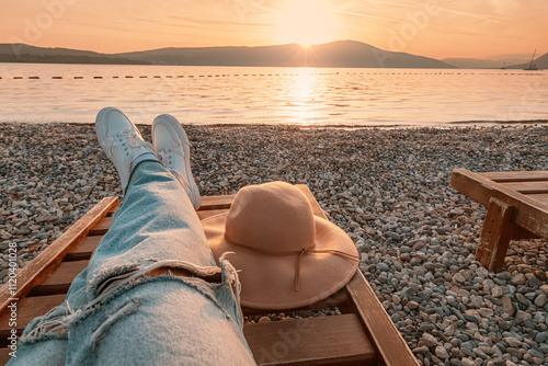 Woman relaxing on deckchair with hat at sunset on pebble beach