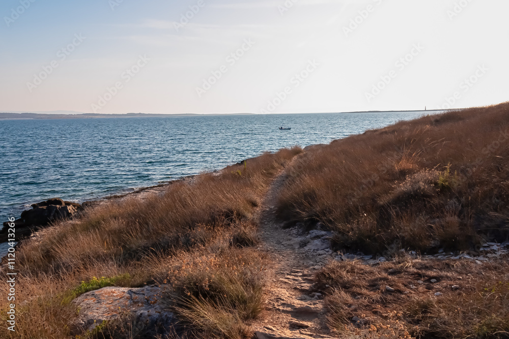 Idyllic coastal hiking trail along rocky shoreline in Cape Kamenjak National Park near Premantura, Istria, Croatia. Calm waters of Adriatic Mediterranean Sea. Hike summer seaside travel destination
