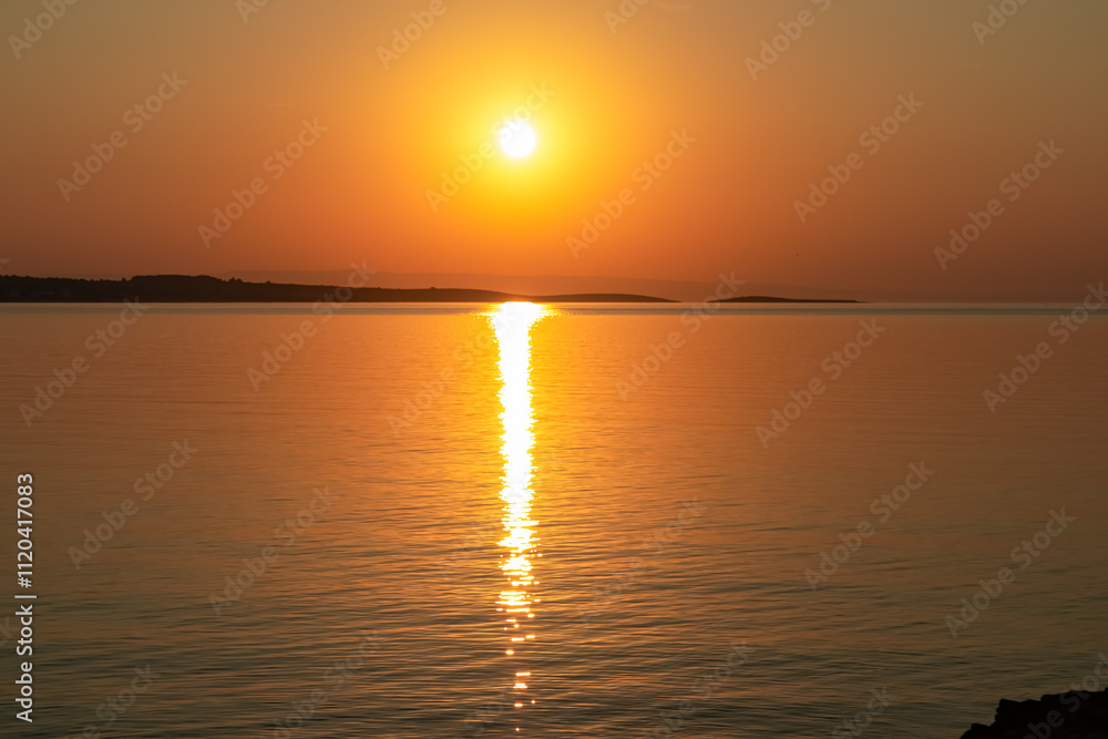 Breathtaking fiery sunset over calm Adriatic Mediterranean Sea in Premantura, Istria peninsula, Croatia, Europe. Reflection of the sun on water creates shimmering path that extends towards horizon Breathtaking fiery sunset over calm Adriatic Mediterranean Sea in Premantura, Istria peninsula, Croatia, Europe. Reflection of the sun on water creates shimmering path that extends towards horizon