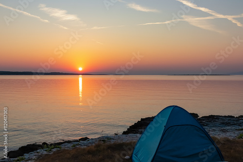 Camping in tent with breathtaking fiery sunset over calm Adriatic Mediterranean Sea in Premantura, Istria peninsula, Croatia. Sun reflection on water creates shimmering path extending towards horizon photo