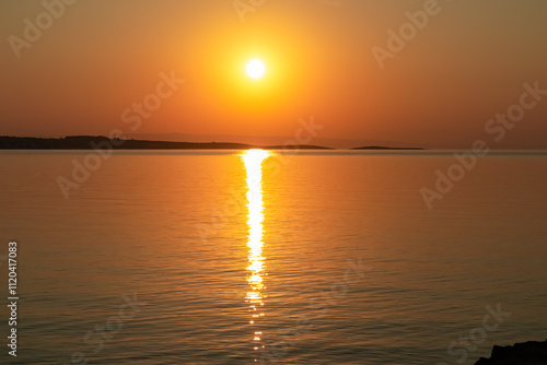 Breathtaking fiery sunset over calm Adriatic Mediterranean Sea in Premantura, Istria peninsula, Croatia, Europe. Reflection of the sun on water creates shimmering path that extends towards horizon photo