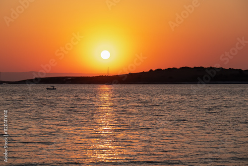 Breathtaking fiery sunset over calm Adriatic Mediterranean Sea in Premantura, Istria peninsula, Croatia, Europe. Reflection of the sun on water creates shimmering path that extends towards horizon photo