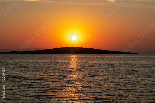 Breathtaking fiery sunset over calm Adriatic Mediterranean Sea in Premantura, Istria peninsula, Croatia, Europe. Reflection of the sun on water creates shimmering path that extends towards horizon photo