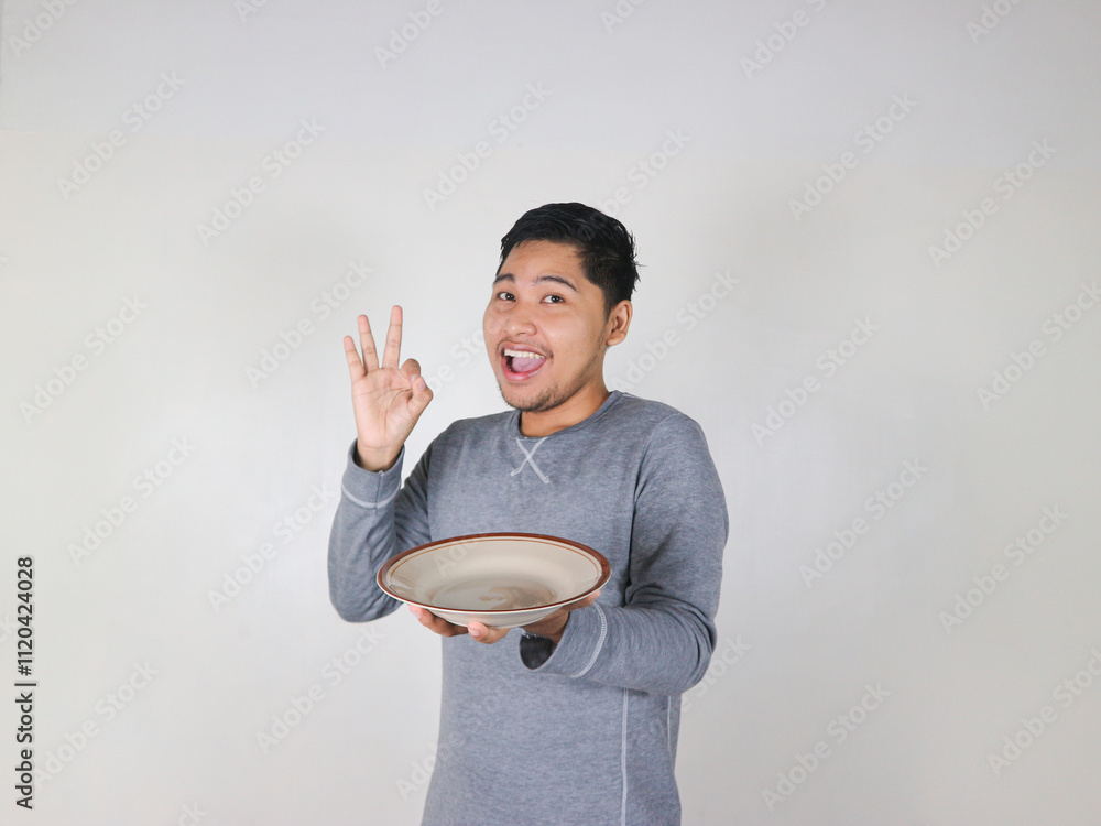 smiling asian man holding empty plate and ok sign smiling asian man holding empty plate and ok sign