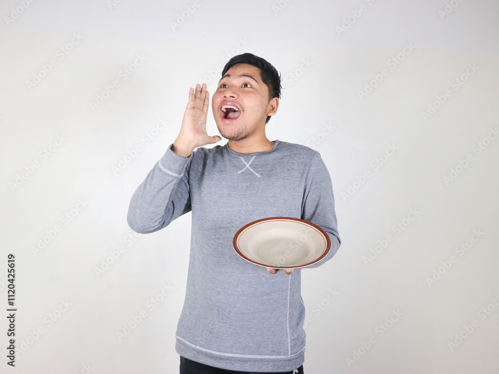 Asian man holding an empty plate while shouting at someone with mouth wide open Asian man holding an empty plate while shouting at someone with mouth wide open
