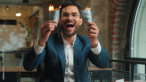 Happy male Arabian Indian business man crazy mad laughing guy joyful excited businessman office investor rejoicing fooling burn money dollars waste finance cash salary enjoy burning banknotes have fun