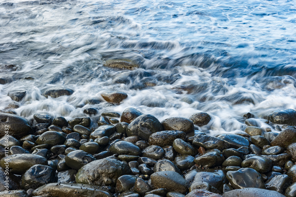 Shallow waves lapping against smooth wet cobblestones on a beach in Maui at sunset Shallow waves lapping against smooth wet cobblestones on a beach in Maui at sunset