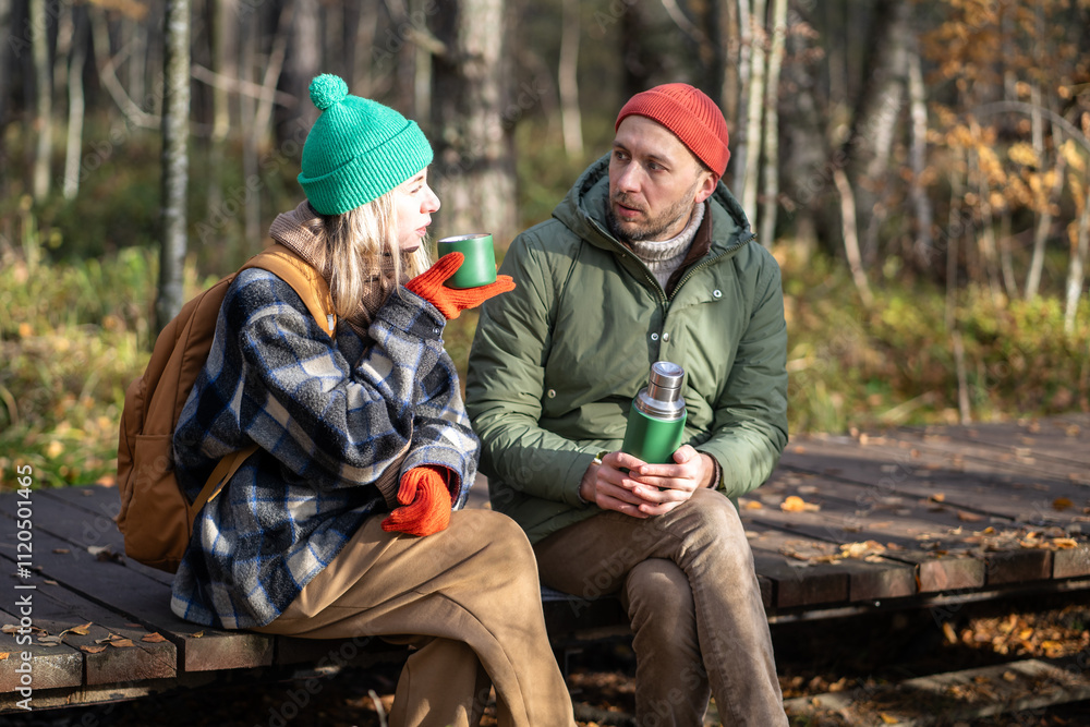 Fototapeta premium Satisfied best friends, hiker travelers sitting on wooden eco path trail through September thicket, talking, chatting, speaking, discussing various topics with interest in pleasant atmosphere.