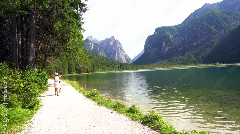 Tourists walking along lake dobbiaco in the dolomites, italy Tourists walking along lake dobbiaco in the dolomites, italy