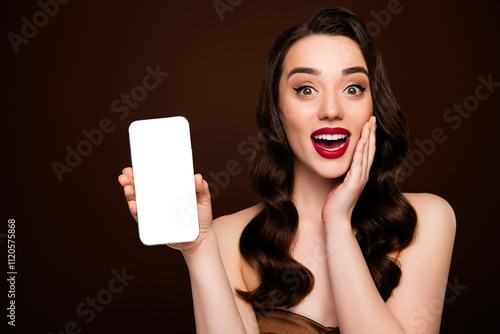 Photo of surprised glamour girl showing empty space screen gadget isolated on brown color background