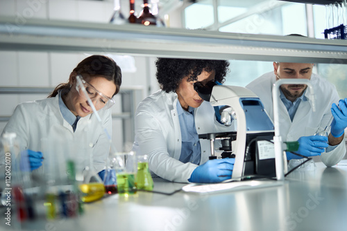 Mid adult female scientist working on a microscope among her colleagues in laboratory.