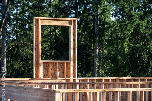 New house construction in progress, glue laminate beam supporting second floor, walls and window wood framing, evergreen trees in background
 photo