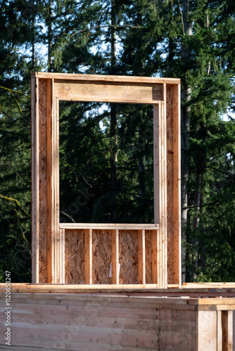 New house construction in progress, glue laminate beam supporting second floor, walls and window wood framing, evergreen trees in background
 photo