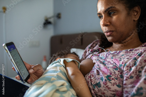 Mother multitasking with smartphone while breastfeeding child photo