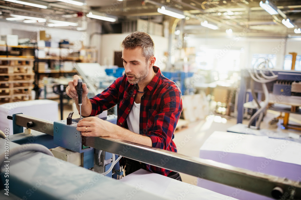 Male technician adjusting machinery in a busy printing press facility Male technician adjusting machinery in a busy printing press facility