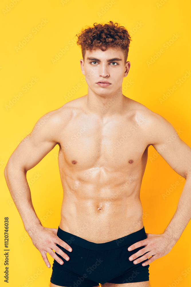 Fototapeta premium Confident young man posing shirtless on a bright yellow background, showcasing his athletic physique. Fitness and self-expression concept.
