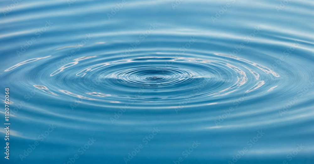 A single water droplet creates concentric ripples on a serene blue surface, capturing the elegance of motion and the tranquility of nature. This image symbolizes simplicity, purity, and the ripple eff A single water droplet creates concentric ripples on a serene blue surface, capturing the elegance of motion and the tranquility of nature. This image symbolizes simplicity, purity, and the ripple eff
