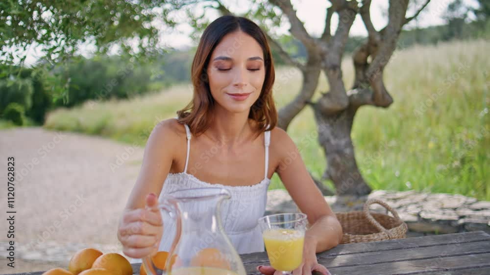 Relaxed girl filling glass with orange juice at nature closeup. Woman drinking