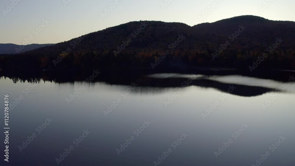 A panoramic shot capturing the serene reflection of forested hills on a calm lake at twilight. The tranquil atmosphere highlights soft evening light and natural beauty. A panoramic shot capturing the serene reflection of forested hills on a calm lake at twilight. The tranquil atmosphere highlights soft evening light and natural beauty.