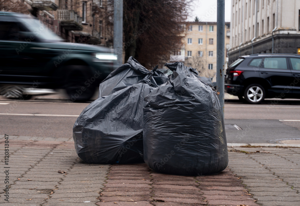 Obraz premium A mountain of dark bags of garbage is waiting to be taken out by the roadside.