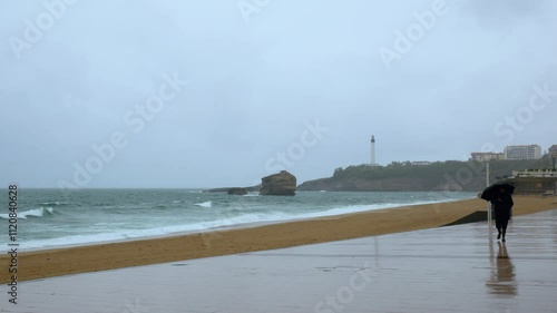 A man walking along the beach of Biarritz under umbrella on a rainy day