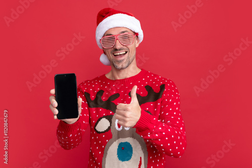 amazed man in sweater and santa claus hat. xmas guy presenting phone screen photo