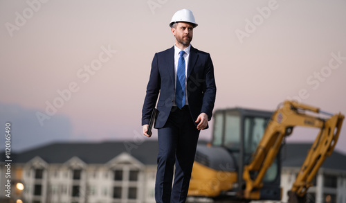 Construction manager in suit and helmet at a construction site. Construction manager worker or supervisor wearing hardhat in front of house. Supervisor construction manager near excavator. Renovation. photo