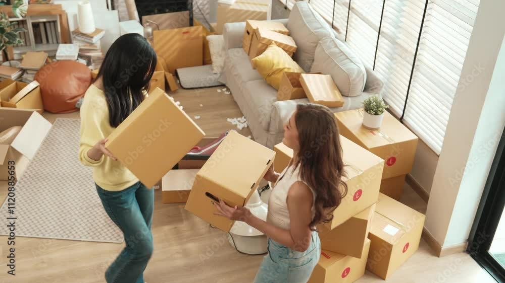Top down view of asian couple holding cardboard box while dancing in to house at moving day. Attractive lesbian couple carrying package while moving in to new house and moving to music. Myrmidon.