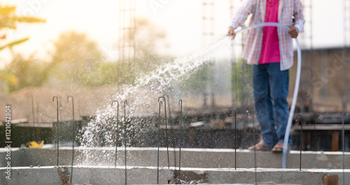 Foto Construction worker watering reinforced concrete beams at a building site, focusing on the curing process for crack prevention, durability enhancement, and protection of reinforced steel structure