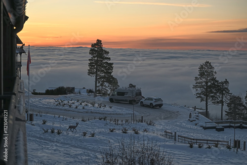 From the Holmenkollen in Oslo you have a sublime view of the fog over Oslo from the mountain and look from above at the clouds with sun above in the depths of winter with snow on roofs and Trees