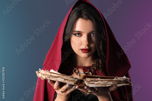 Young witch with spell book on dark color background photo