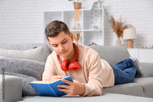 Teenage boy with headphones doing homework on sofa at home photo