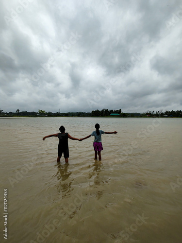 Silhouette of Two People Walking in Flooded Water Under Dramatic Cloudy Sky