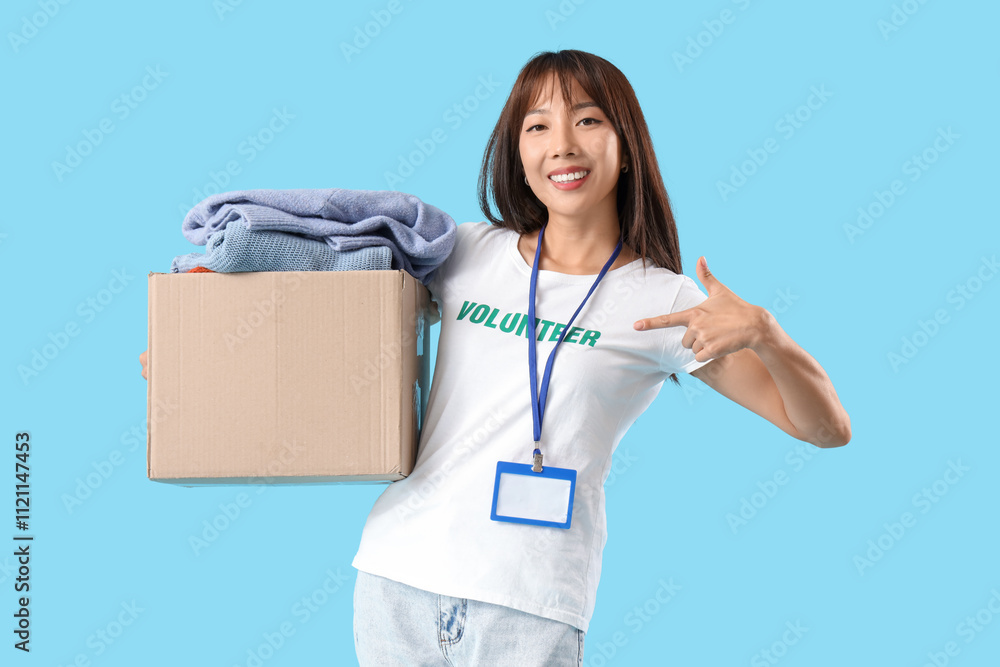 Young female volunteer with donations on blue background Young female volunteer with donations on blue background