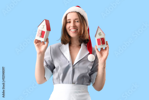 Young chambermaid with Santa hat and advent calendar on blue background