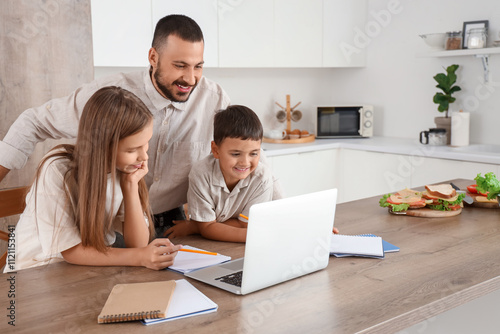 Cute little children with their father doing homework in kitchen at home