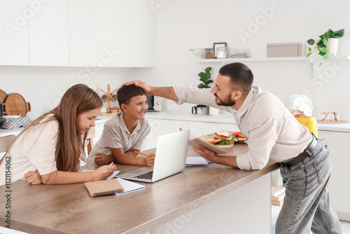 Cute little children with their father doing homework in kitchen at home