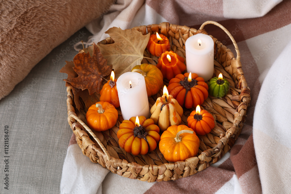 Wicker tray with glowing candles and autumn leaves on sofa in room Wicker tray with glowing candles and autumn leaves on sofa in room