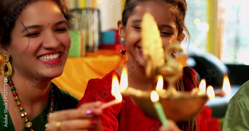 Closeup of Happy Indian Family of Four in Traditional Attire Lighting Diya or Samai Together on Hindu Festival Day at home photo