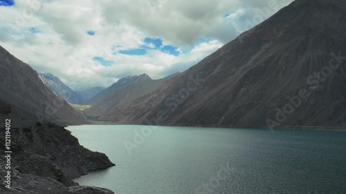 Landscape view of Satpara Lake surrounded by mountains with rocky shore and cloudy sky photo