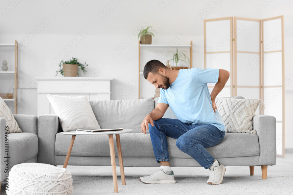 Young man suffering from back pain on sofa at home Young man suffering from back pain on sofa at home