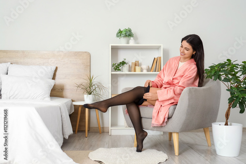 Pretty young woman putting on black tights in bedroom photo