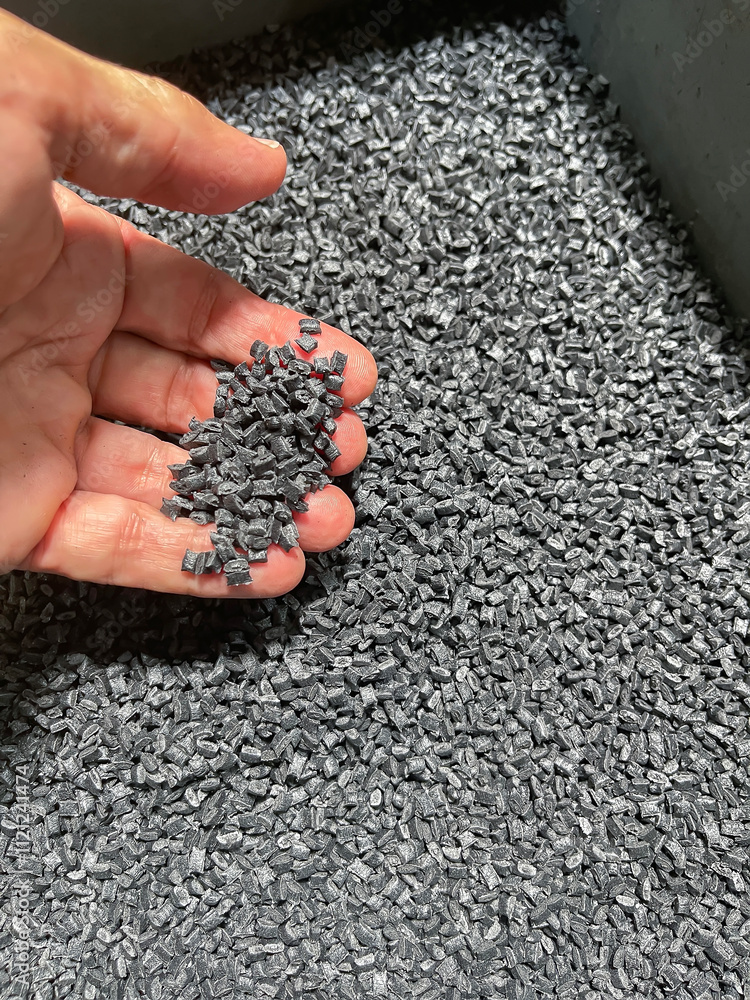 plastic raw material, hand holding a handful of black plastic pellets on a gray plastic drawer, production of plastic parts, plastic injection, spilling of plastic grains with glass fiber