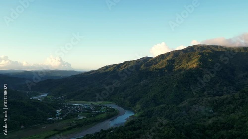 Aerial overview of sunset-covered mountains along lush tropical valley and river with village in San Miguel, Catanduanes, Philippines. photo